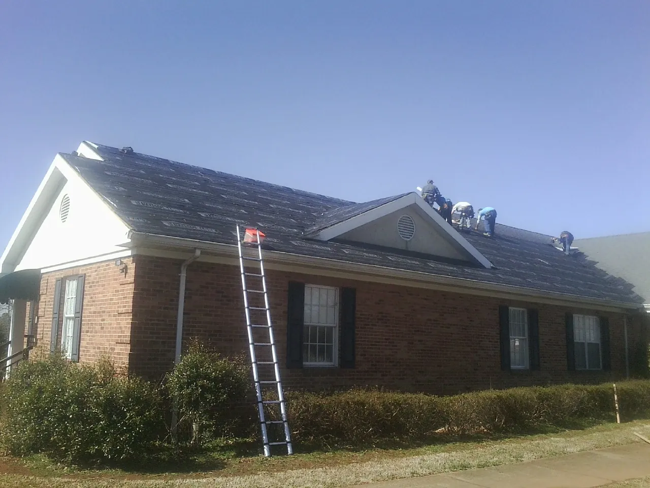Crew tearing shingles off a brick ranch roof with a ladder set — Metal Roof Repair work by our crew in Tenino