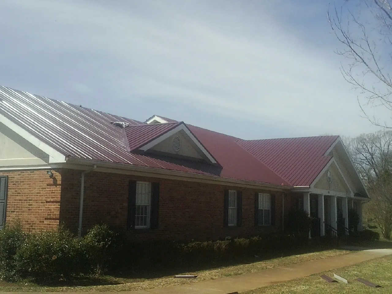 Red metal roof with gabled entries on a long brick building, from a Hail Damage Roof Repair job in Tenino