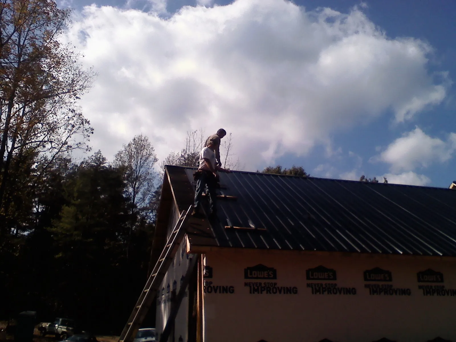 Roofer fastening dark metal panels high against a cloudy sky, from a Roof Inspection job in Tenino