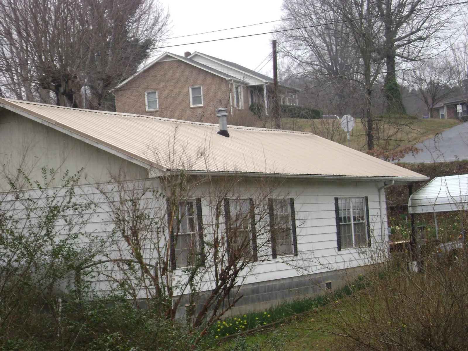 Tan metal roof on a white sided house set into a hillside — Commercial Roofing by Roofing Brothers in Tenino